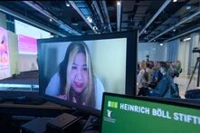 Person live per Video zugeschalten redet, Podium im Hintergrund