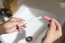 Safe Abortion Day Ein Schwangerschaftstest ist positiv ausgefallen. Zwei weisse weibliche Hände halten ihn über einem sonnenbeschienen Waschbecken. Es wirkt wie eine Point-of-View-Aufnahme.