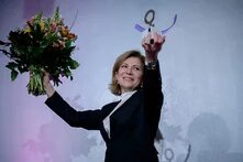 Joumana Seif hält den Anne-Klein-Frauenpreis in einer Hand und einen Blumenstrauß in der anderen. Sie lächelt vor einem neutralen Hintergrund.