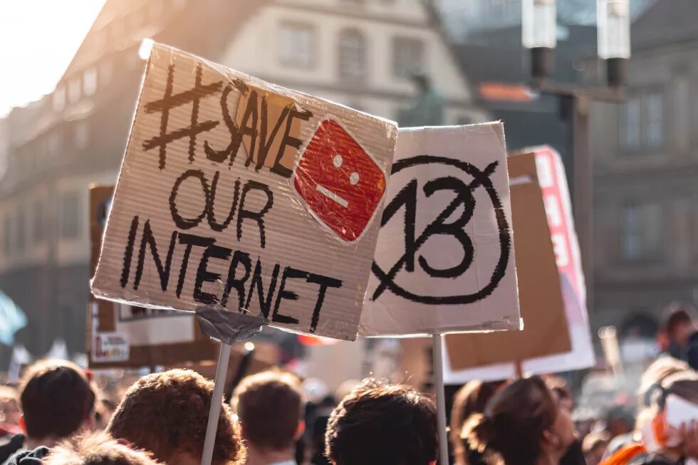 someone holding a poster on a demonstration with the words "#save our internet" written on it