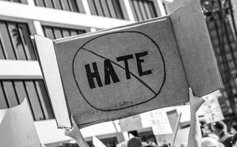 someone holding a poster at a demonstration with the word "hate" crossed out on it