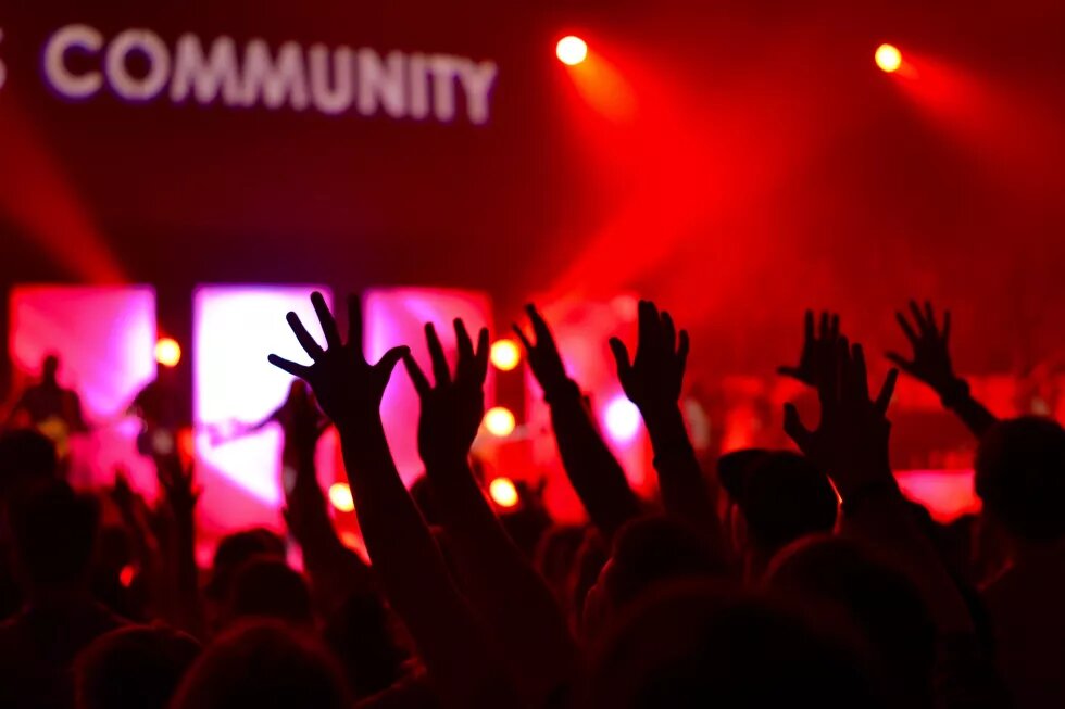 people raising their hands in a club, abova a sign that says "community"