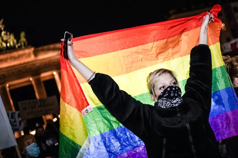 masked person demonstrating, holding a rainbow flag