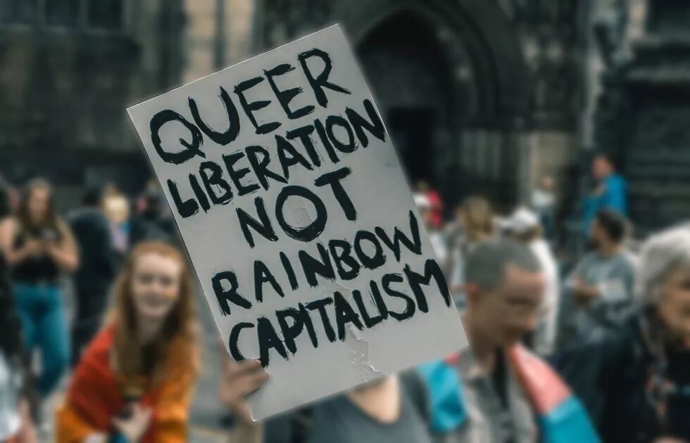 Eine Person hält ein Schild auf dem "queer liberation not rainbow capitalism" steht