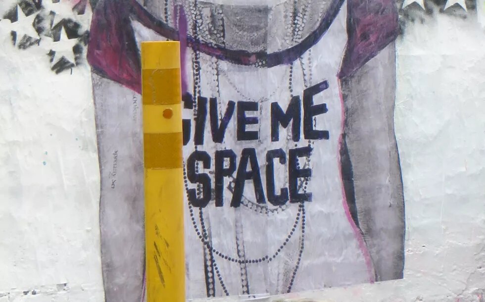 Streetart mit dem Text "Give me space" auf dem weissen T-Shirt einer Person. 