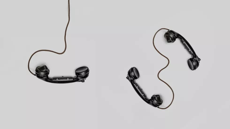 Drei schwarze Telefonhörer mit Kabel vor grauem Hintergrund