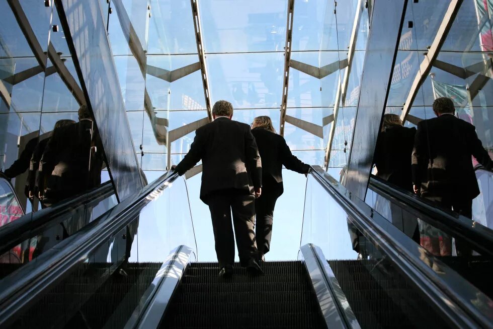 Mann udn Frau in Businesskleidung auf einer Rolltreppe, auf dem Weg nach oben.