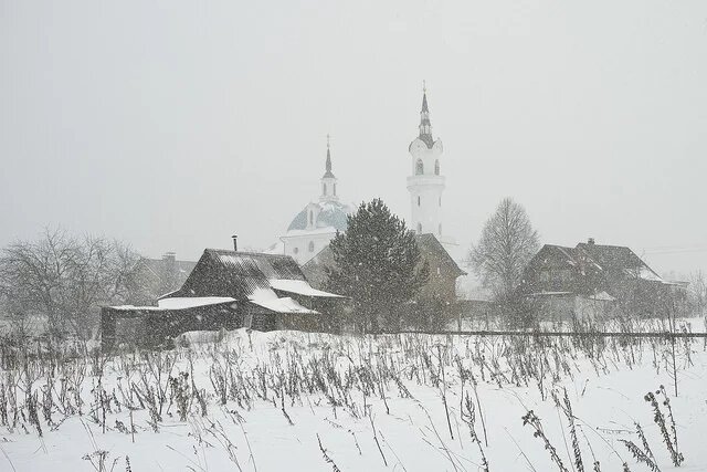 The Church of Archangel Michael in Podzhigorodovo Russian village houses, barns and a church through a snow shower
