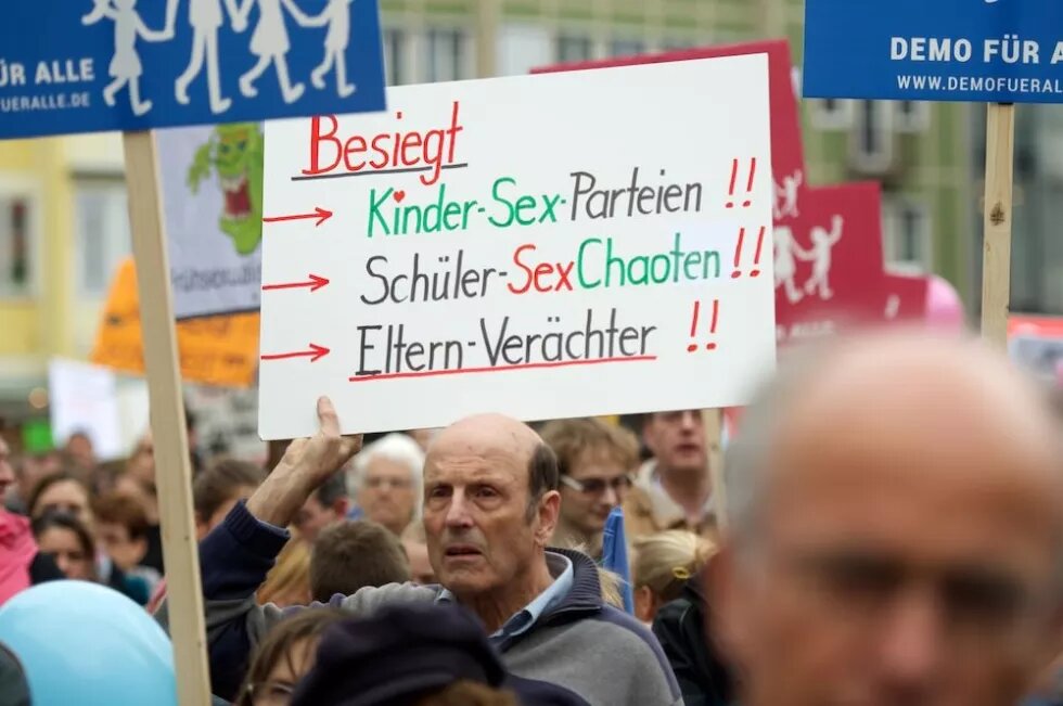 Ein Demonstrant hält ein Schild hoch, auf dem steht: Besiegt Kinder-Sex-Parteien, chüler-Sex-Chaoten, Eltern-Verächter