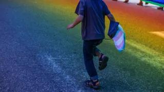 trans Schwangerschaft Junge Person laeuft mit Transflagge auf Asphalt, der in Regenbogenfarben scheint