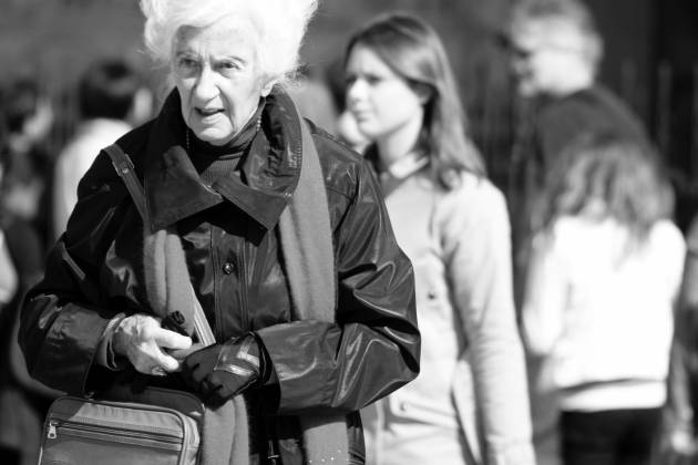 Pflege und Migration in Europa schwarz-weiß Portrait einer alten Frau, im Hintergrund junge Menschen