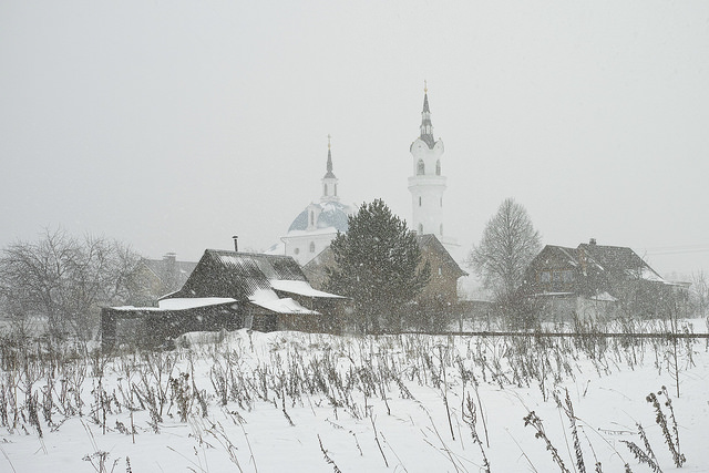The Church of Archangel Michael in Podzhigorodovo Häuser, Scheunen und Kirche eines russischen Dorfes im Schneeschauer