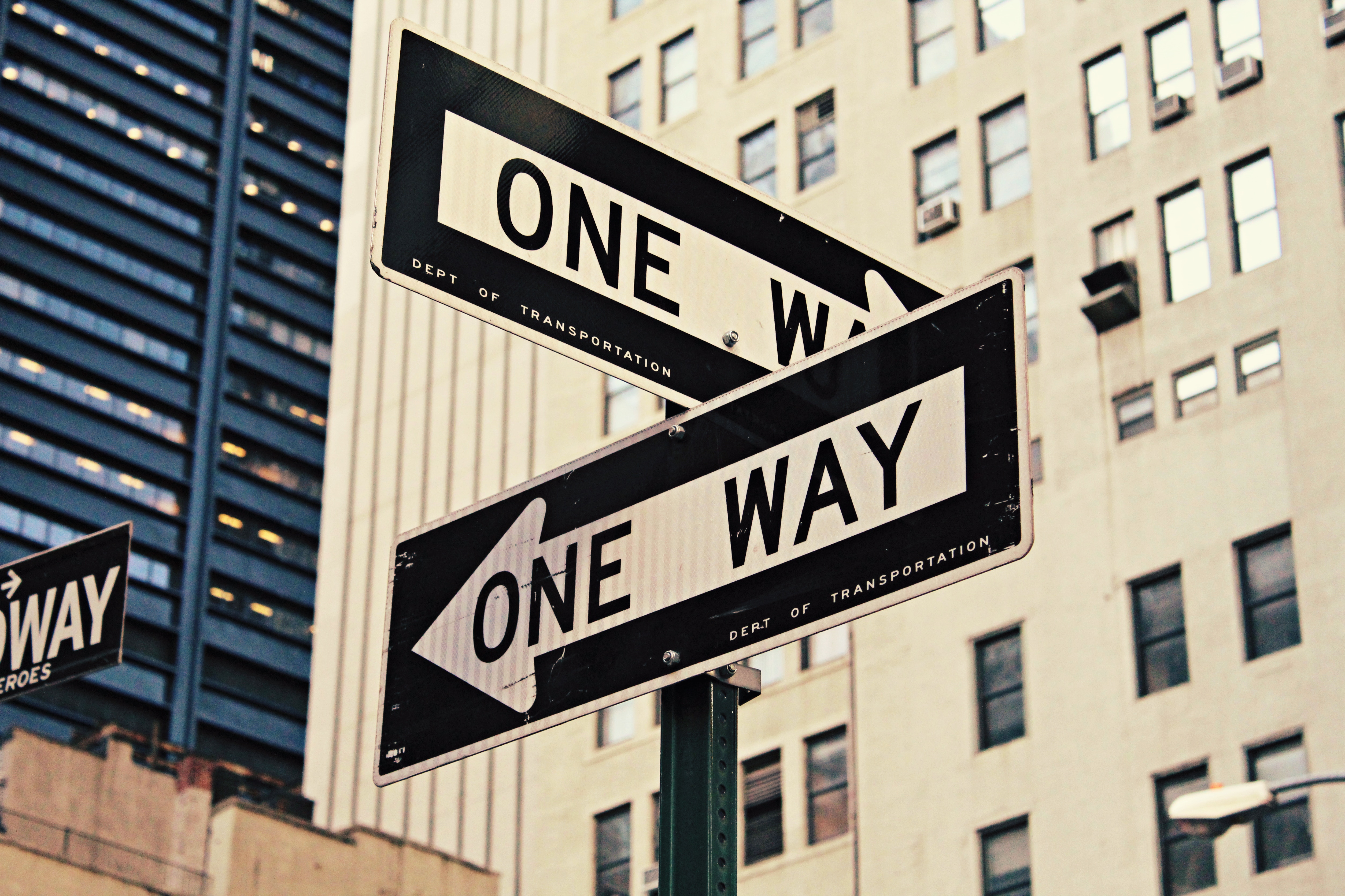 One Way Foto einer Kreuzung in New York. Zwei Straßenschilder mit "One Way"-Aufschrift weisen in verschiedene Richtungen.